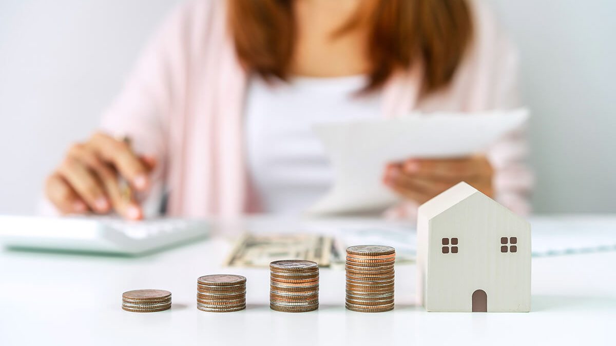 Mujer calculando el impuesto de inmueble con monedas y modelo de casa