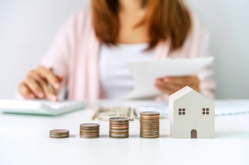 Mujer calculando el impuesto de inmueble con monedas y modelo de casa